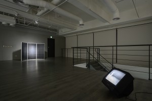 Exhibition view of the solar panel and a TV screen that has a black and white image of a person in a landscape. 